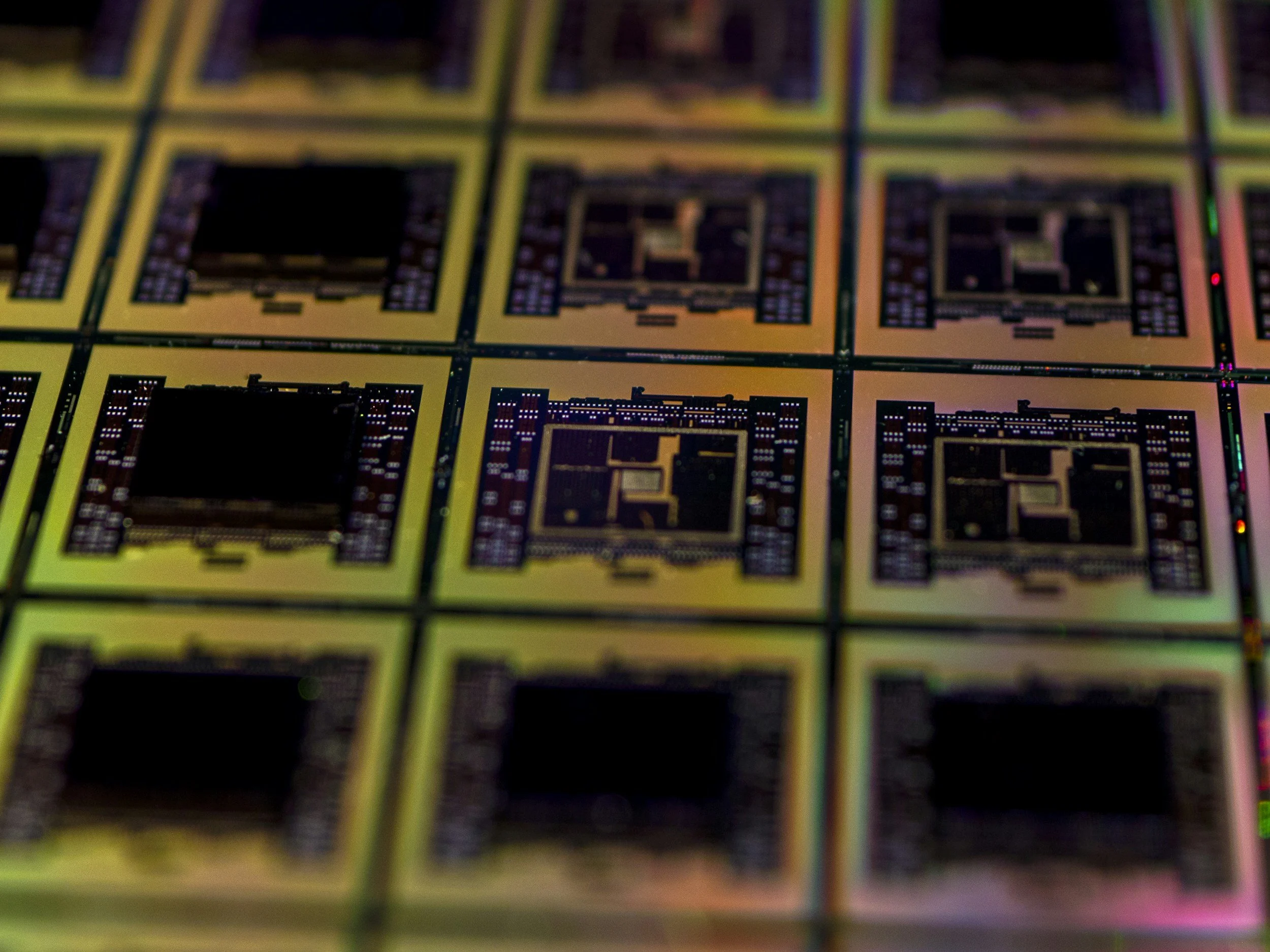 Close-up of multiple semiconductor chips with a reflective, holographic surface, arranged in a grid pattern.